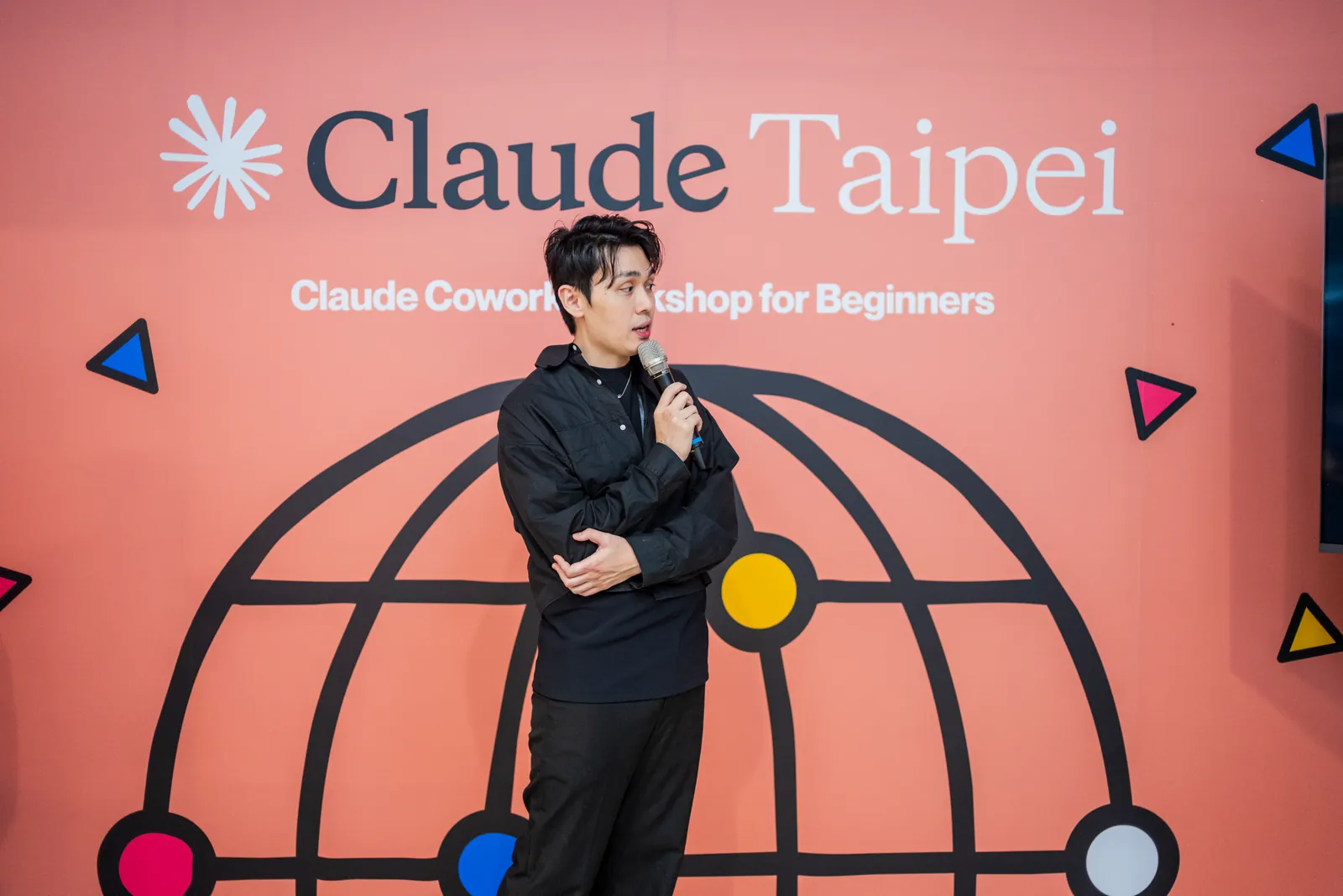 Dawson Wang 在 Claude Cowork for Beginner 活動上拿著麥克風分享,背後是 Claude Taipei 的粉紅色地球背板