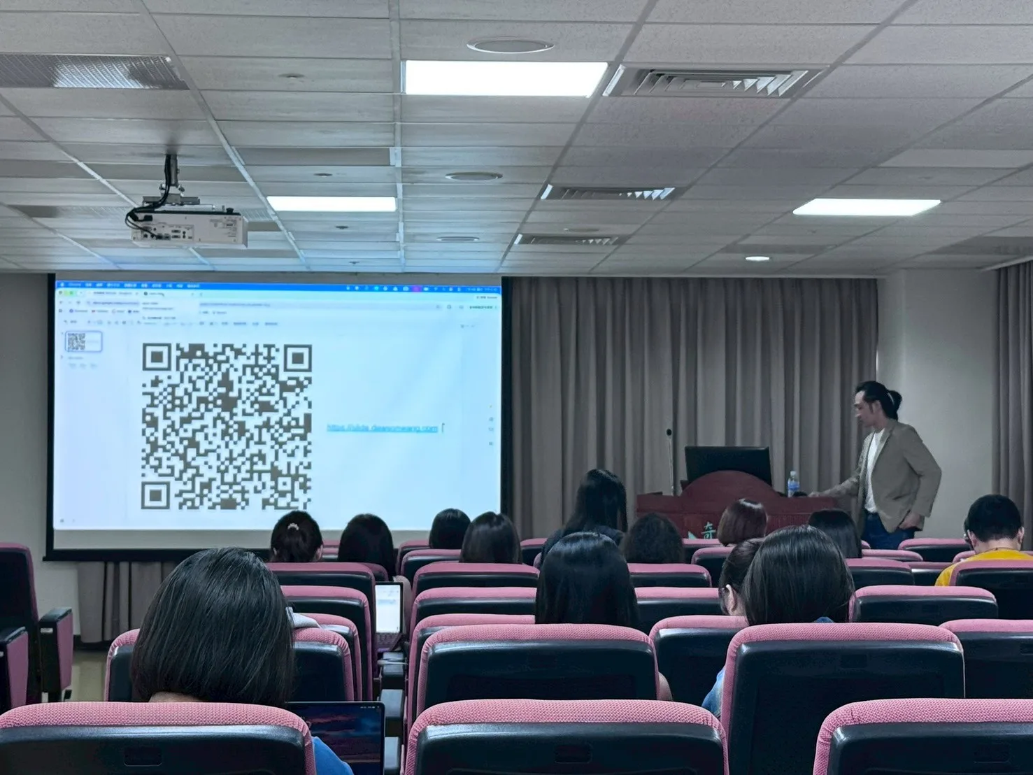 奇美醫院總院講堂內，Dawson Wang 在大型 QR code 投影旁帶領現場實作